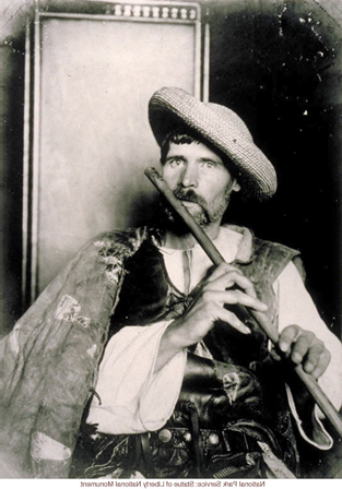 This image is labeled 'Eastern European Immigrant,' and the picture shows a young man with a beard, a woven hat with a wide brim angled to the side of his head. He wears a sort of cape, a vest, and a white shirt tied at the neck. He plays a flute that he holds in front of him.